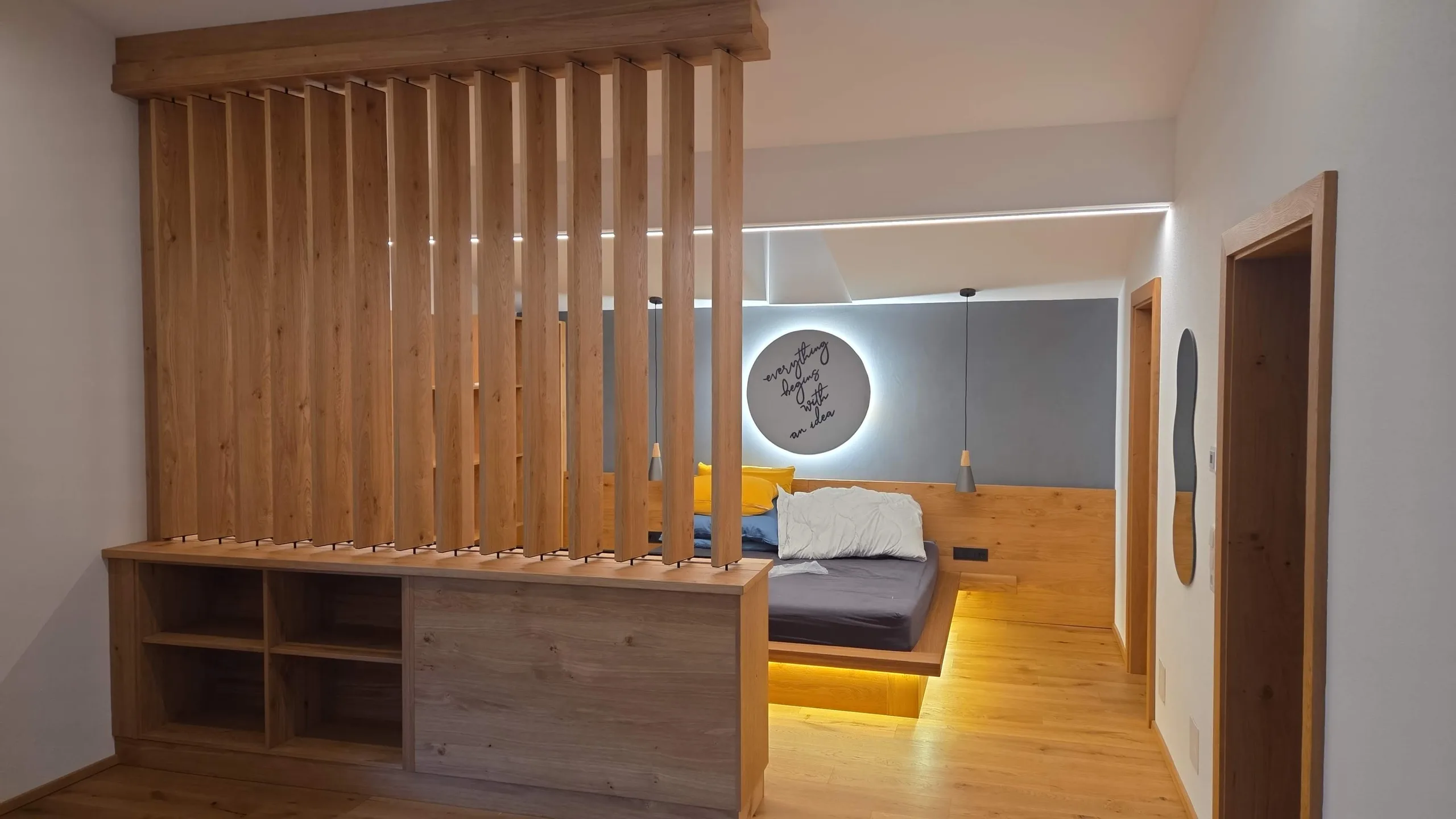 Blick durch den drehbaren Lamellen-Raumteiler auf das Kingsize-Bett