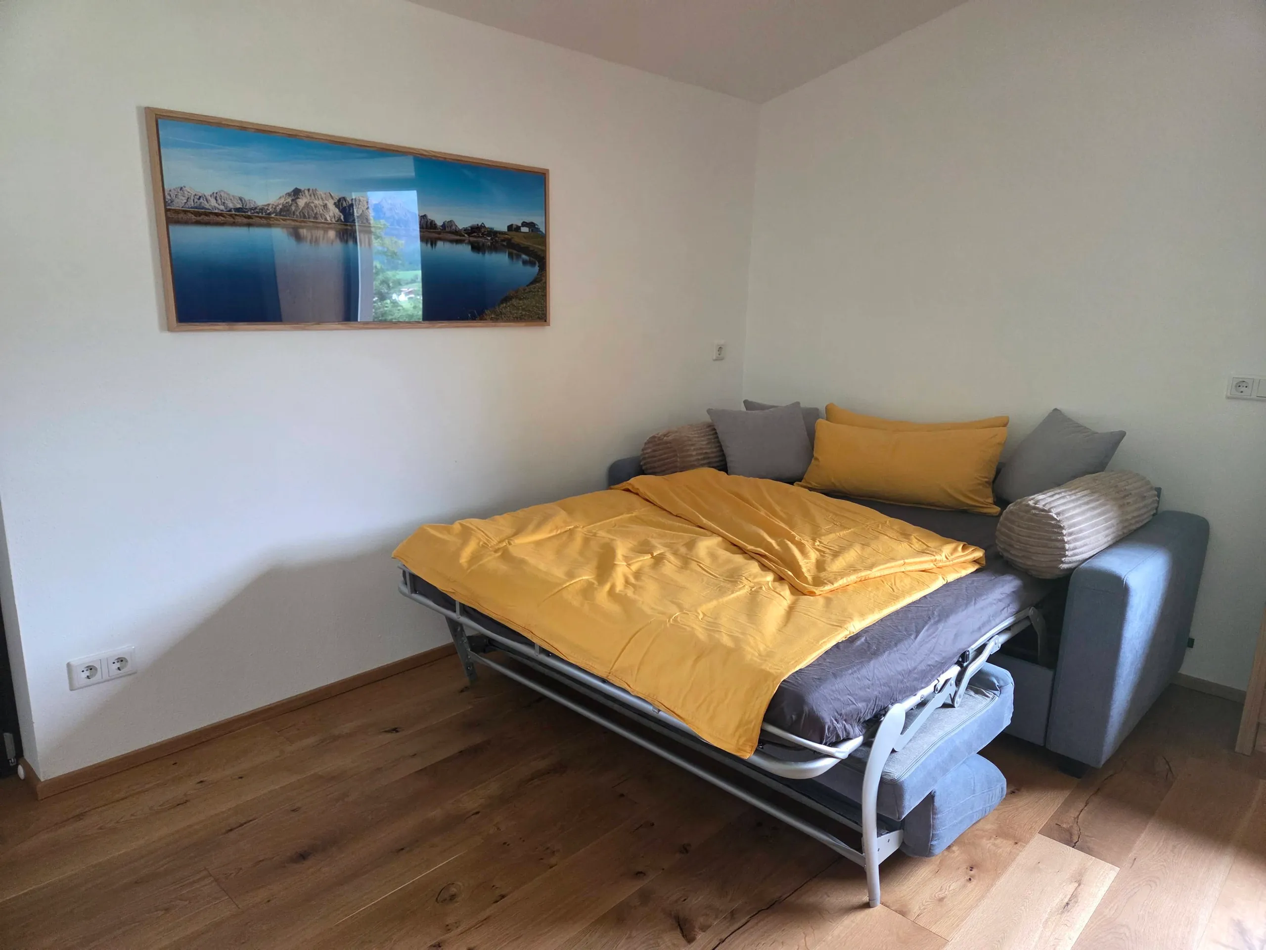 Zum Queensize-Bett ausgeklappte und bezogene Schlafcouch, darüber ein Bild vom Bergsee